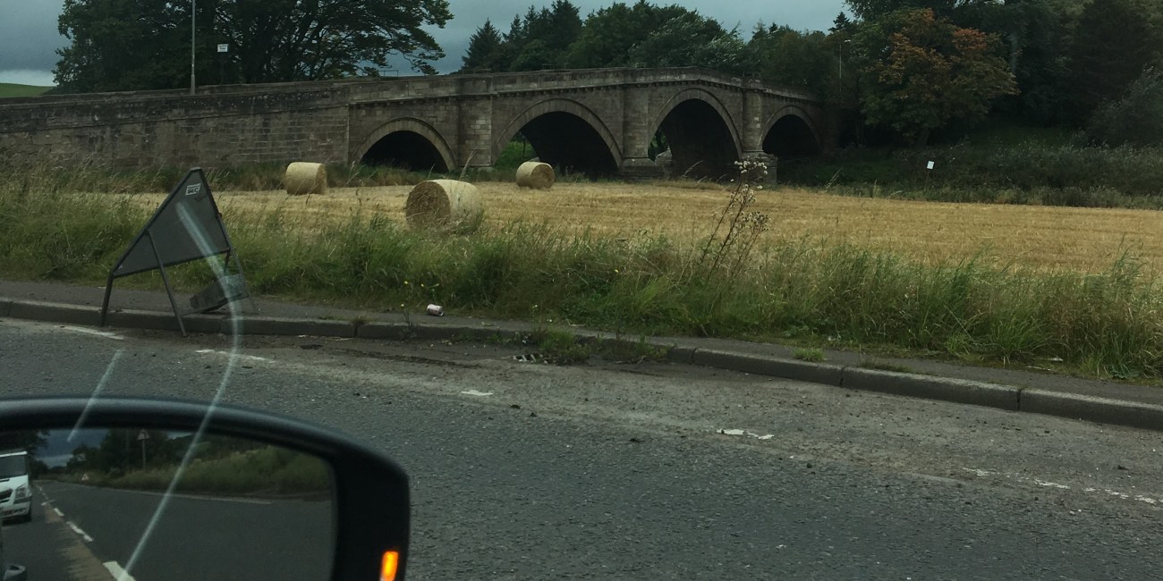 One Health approach Preparing for the unknown banner image - Roadside view from a car of a bridge and hay bails in a field