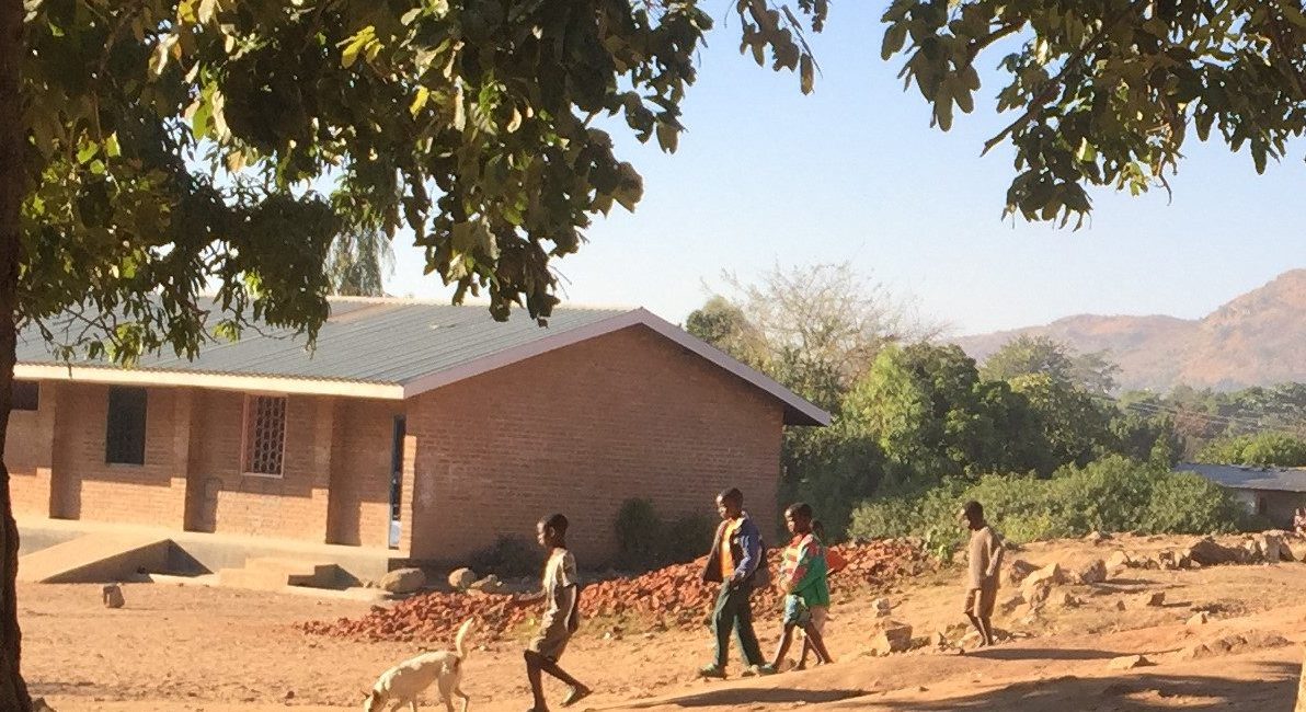 Village seen through trees, with children walking down a small hill with a dog